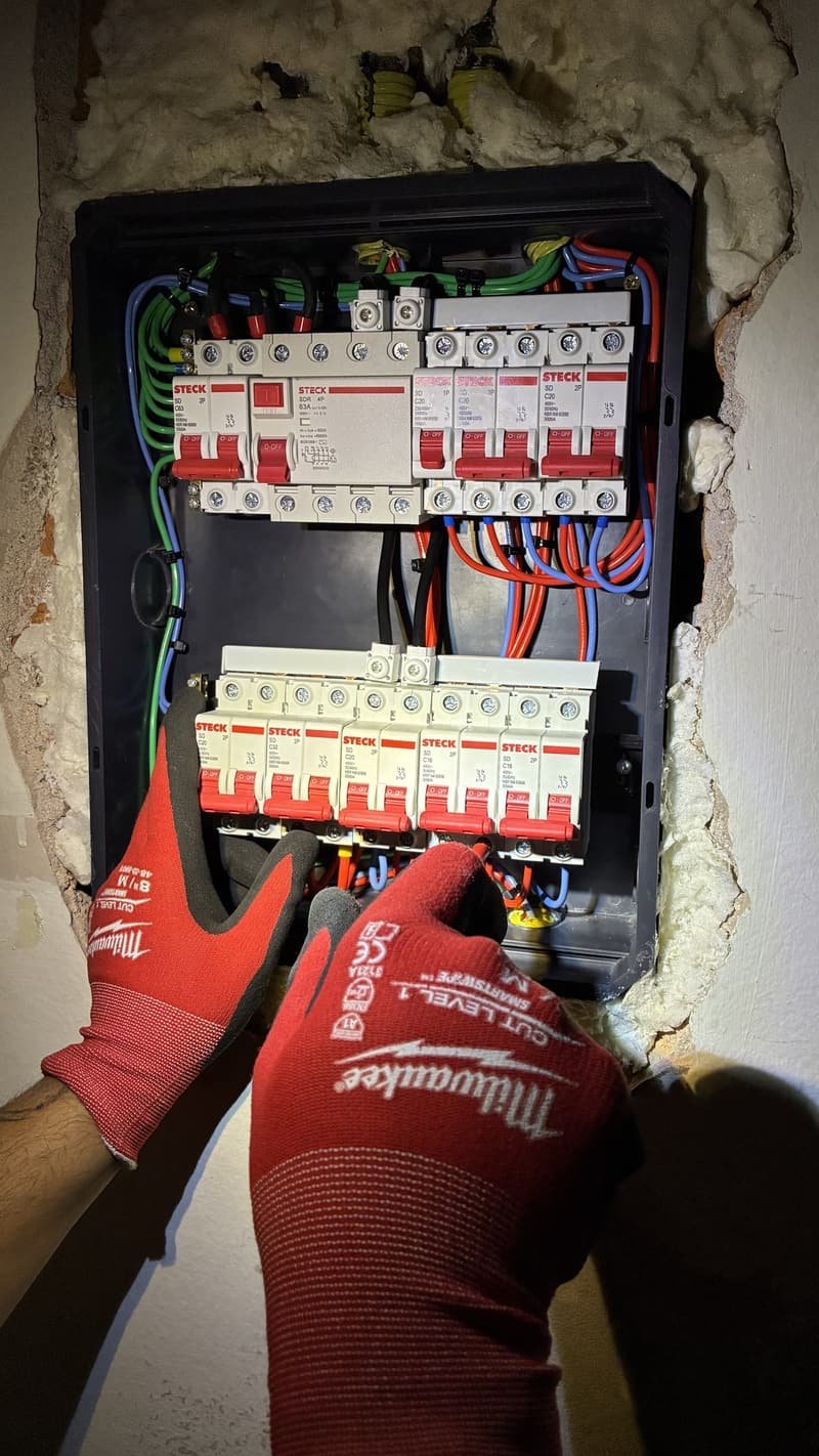 Mãos com luvas de proteção trabalhando nos disjuntores de um quadro elétrico