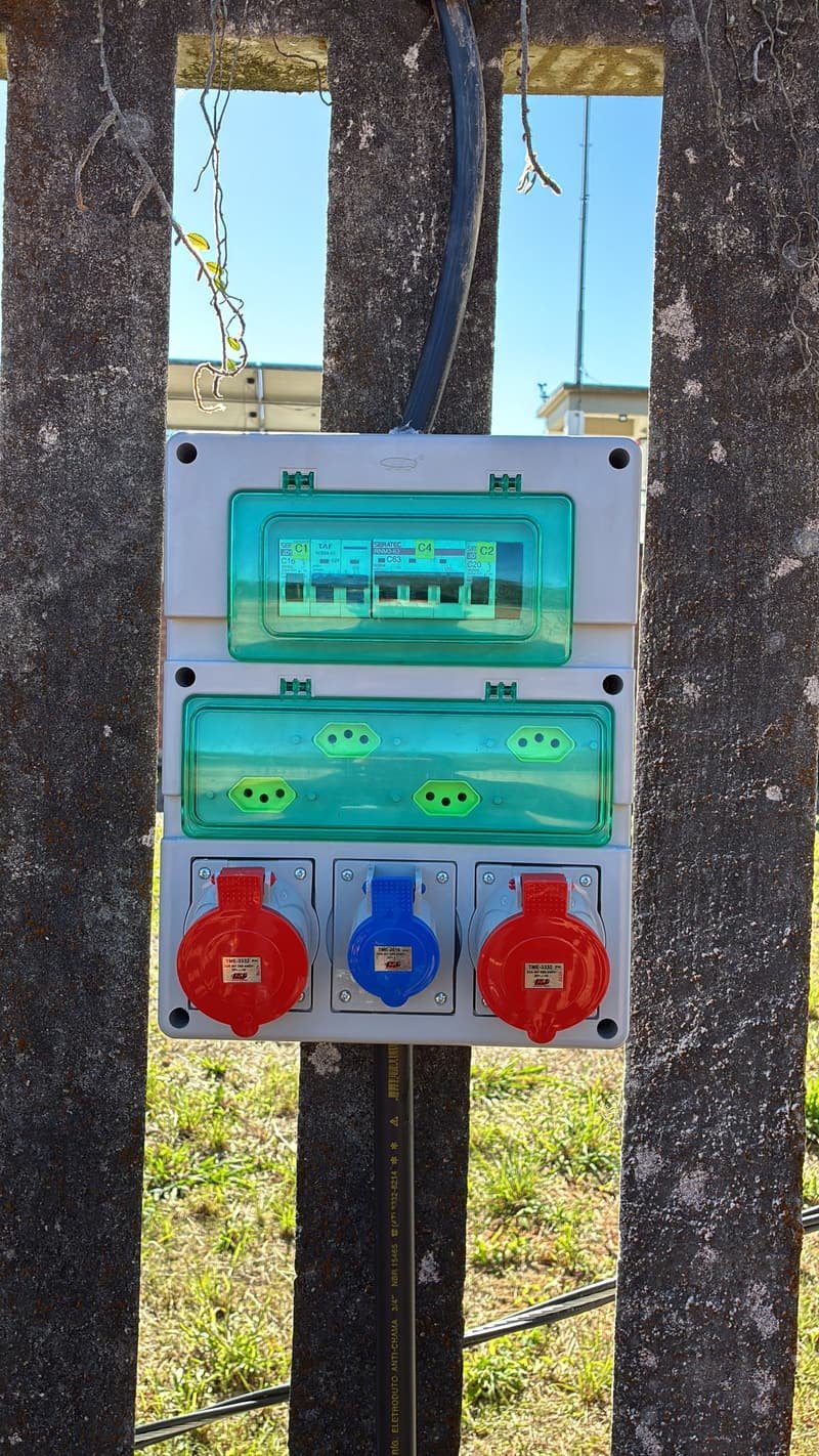 Quadro externo com disjuntores e três tomadas industriais, instalado em estrutura de madeira